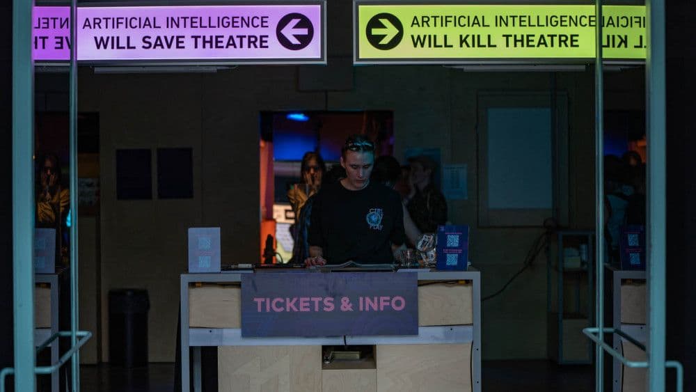 Een vrouw staat achter een ticketbalie. Boven haar hangt een bord met een pijl naar links en de tekst 'artificial intelligence will save theatre' en een bord met een pijl naar rechts en de tekst 'artificial intelligence will kill theatre'. Mensen kunnen bij het naar binnengaan een richting en dus antwoord kiezen.